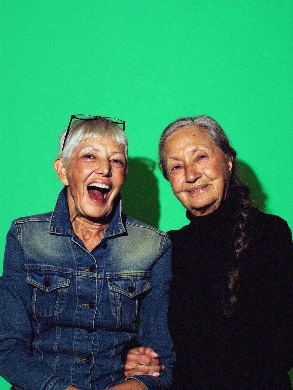 Two friends laughing together against a mint green backdrop