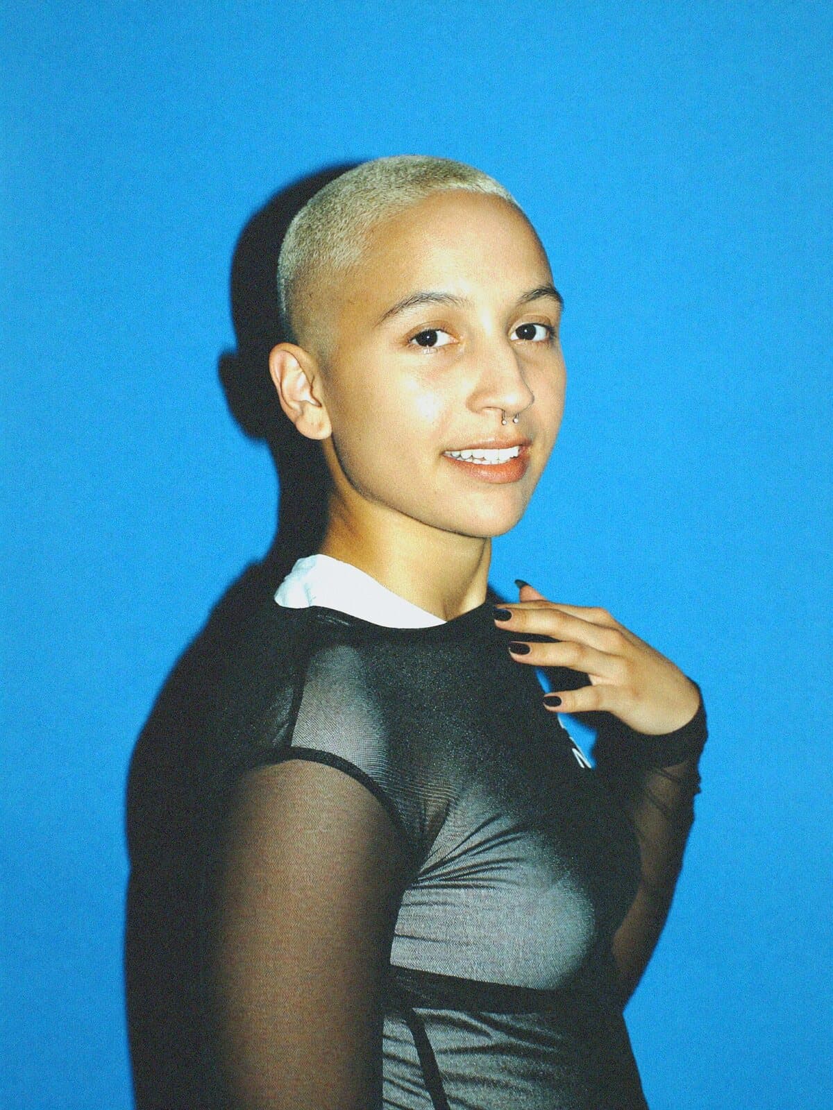 A person with a bleached buzz cut against a sky blue backdrop